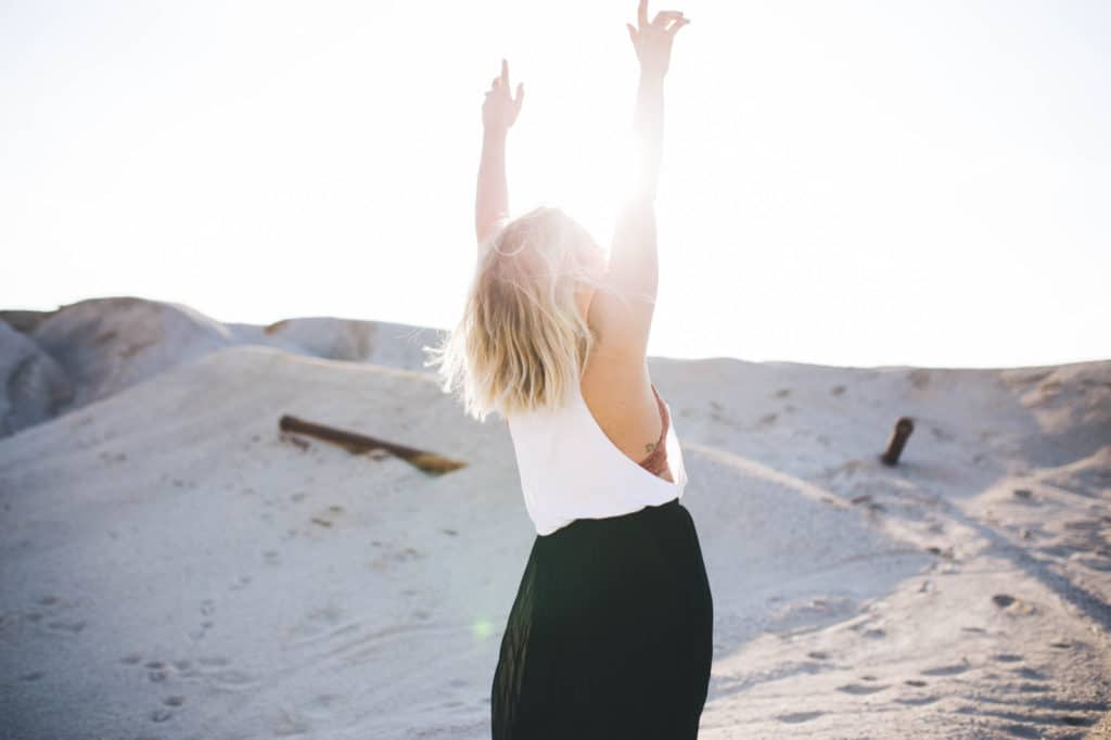 Healing from Chronic Illness - Woman in desert with hands raised toward the sun
